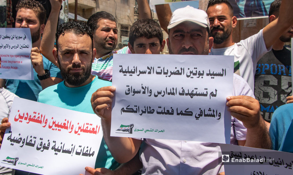 A man carrying a sign in which he addresses the Russian President Vladimir Putin. The sign says (Mr. Putin, the Israeli strikes did not target the schools, markets, and hospitals as the Russian warplanes did) – 03 July 2020 (Enab Baladi / Anas al-Khouli)