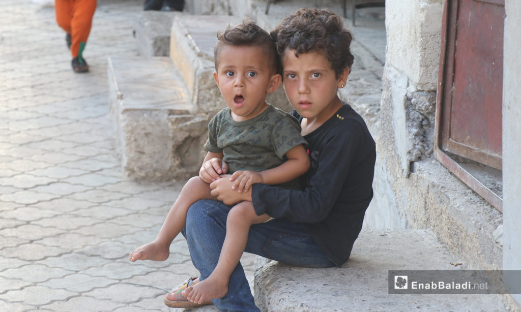 A child holding her little brother in front of their house in al-Raqqa city - 26 July 2020 (Enab Baladi / Abdul Aziz Saleh)