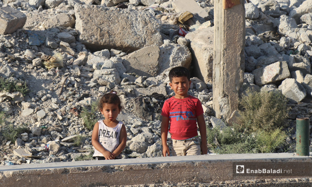 Two children standing in front of a destroyed building in al-Raqqa city - 26 July 2020 (Enab Baladi / Abdul Aziz Saleh)