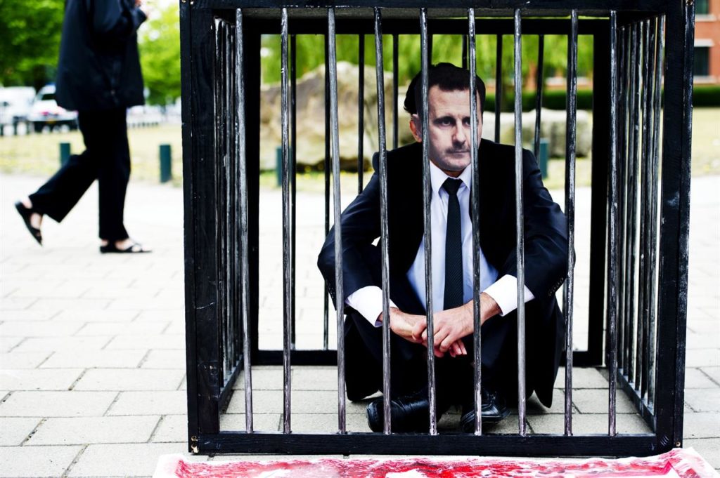 A protester wearing a mask of the President of the Syrian regime, Bashar al-Assad, sits on the ground inside the dock in front of the International Criminal Court in The Hague, western Netherlands - June 7, 2011 (ROBIN UTRECHT / ANP / AFP)