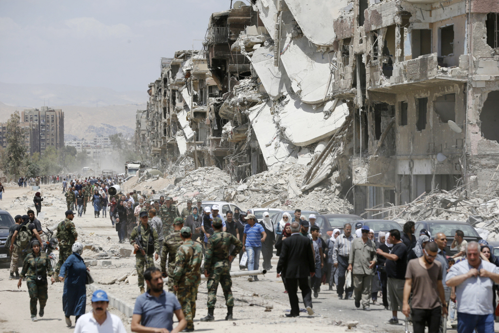 Civilians and forces affiliated to the Syrian regime's government walking in the destroyed 30th Street in the Yarmouk camp - 24 May 2018 (AFP)