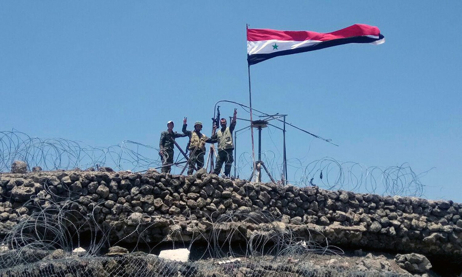 Regime forces soldiers making the victory sign next to the Syrian regime's flag in Tell al-Harrah on the highest hill in the southwestern governorate of Daraa - July (AFP)