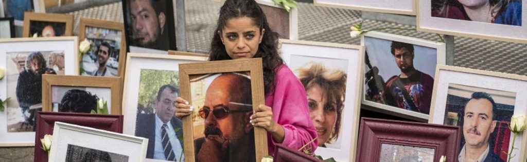 Wafa Mustafa sits between pictures of victims of the Syrian regime as she holds a picture of her father, outside the Koblenz Court building, west of Germany— 4 June 2020 (AFP/Thomas Lohnes)