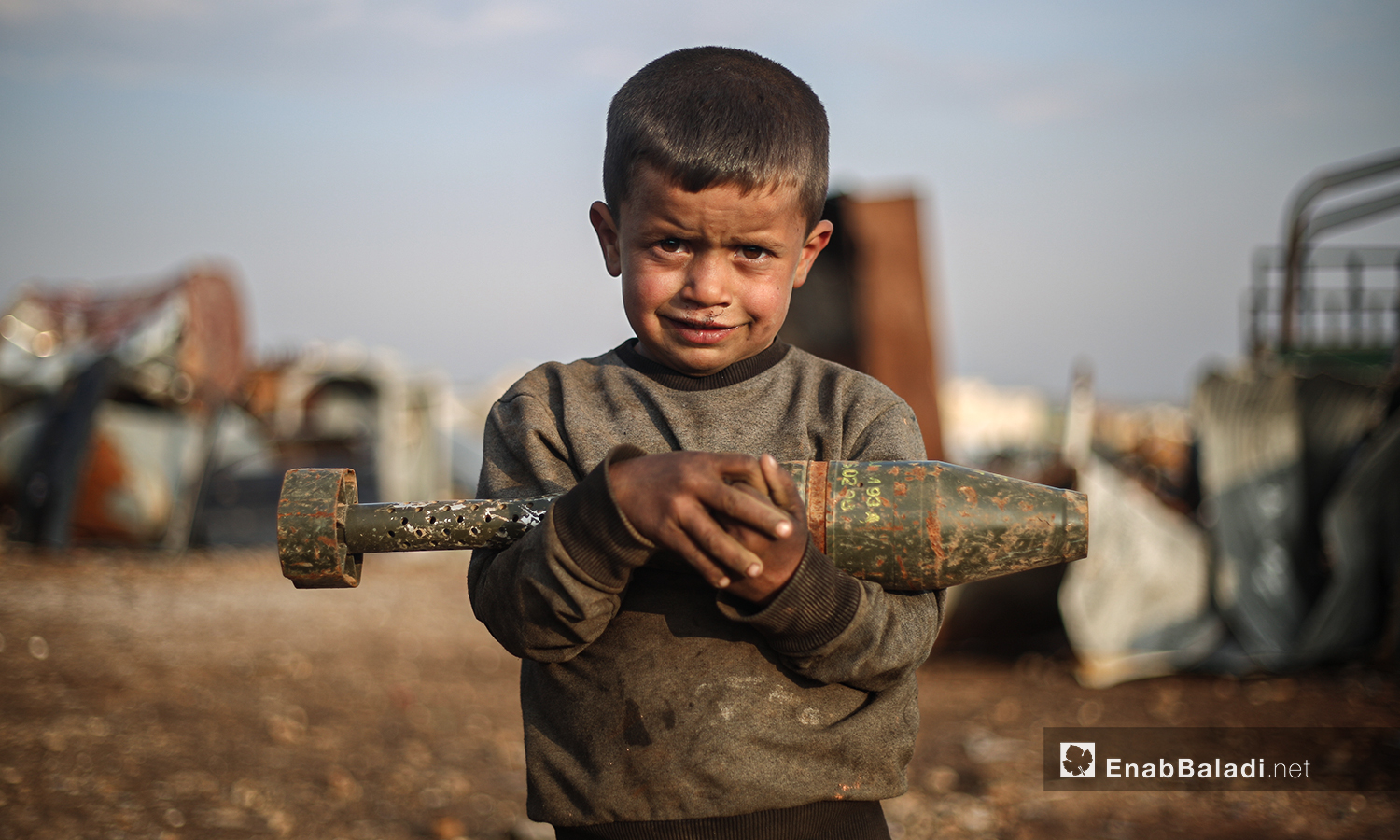 The child carries an unexploded artillery shell in the recyclable rocket collection yard in the northern countryside of Idlib.  He works with his family to secure their livelihood from the killing tool that caused the death of tens of thousands of children during Syria’s ten years of war - 5 March 2021 (Enab Baladi / Youssef Gharibi)
