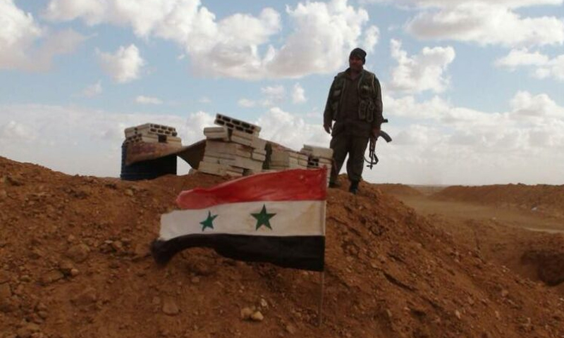 A soldier from the Syrian regime forces standing near the regime’s flag - (NGUOIDUATIN)