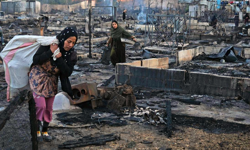 Two Syrian refugee women walking through the remains of a burnt camp in northern Lebanon (AFP)