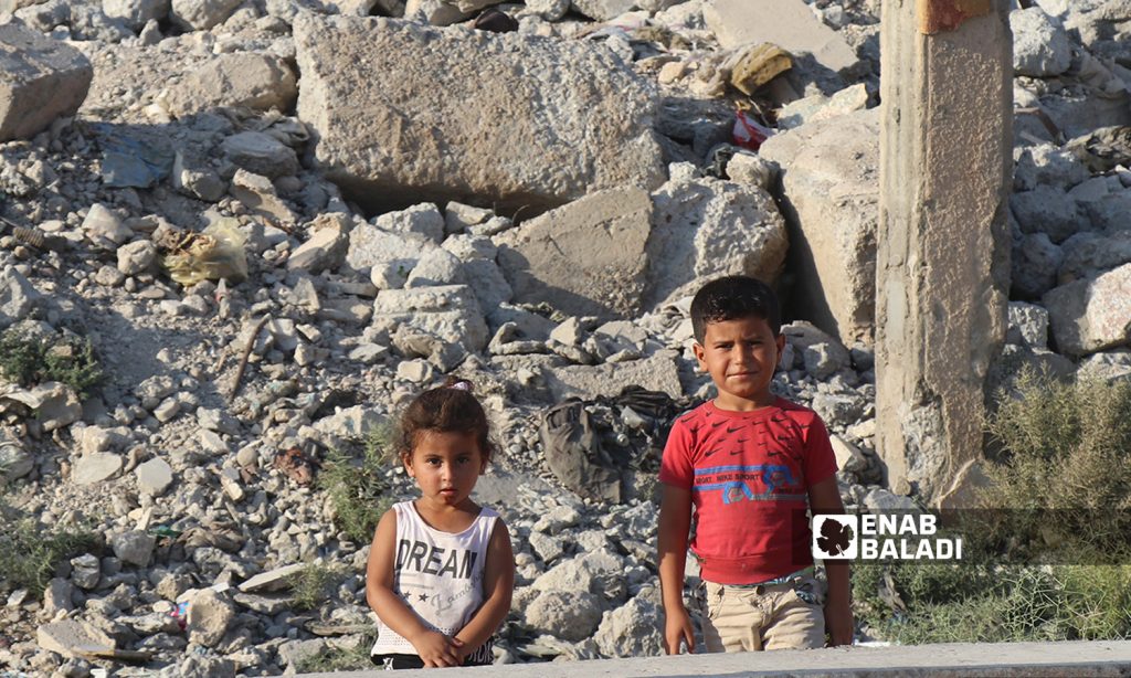 Two Syrian children standing in front of a destroyed building in Raqqa city in northeast Syria - 26 July 2020 (Enab Baladi / Abdul Aziz al-Saleh)