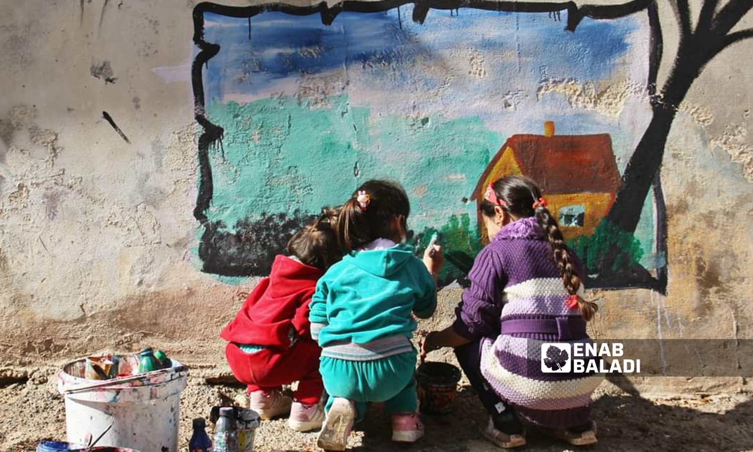 Syrian graffiti artist Aziz al-Asmar painting a mural of a house with the help of children on a wall in Binnish city in Idlib - 2019 (Enab Baladi)