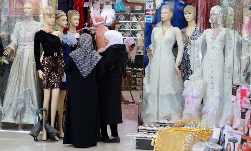 Syrian women looking at dresses displayed in front of a clothing shop in Souq al-Hamidiyah in Damascus old city - 3 December 2019 (AFP)