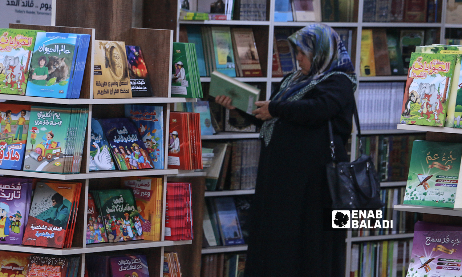 A woman examining a book at Idlib’s book fair- 6 September 2021 (Enab Baladi / Anas al-Khouli)