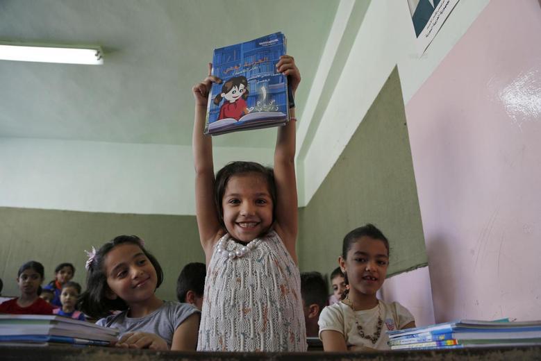 A girl cheerfully showing her book at a school in Damascus (Reuters)