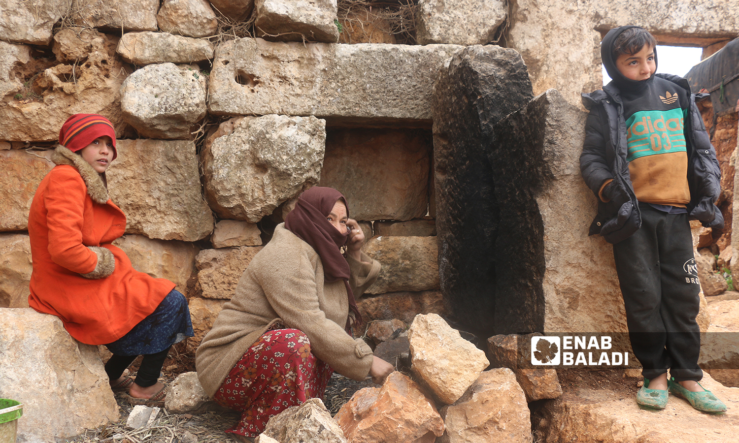 A displaced Syrian woman setting up fire near an archeological site in the historical Sarjableh area in the northern countryside of Idlib governorate - 22 January 2022 (Enab Baladi / Iyad Abdul Jawad)
