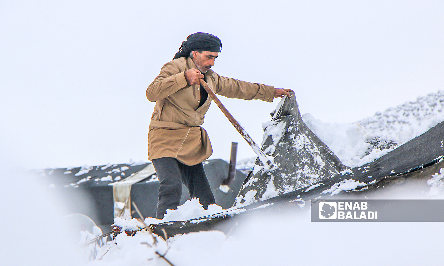 Displaced Syrians clear accumulated snow off the roof of their tents following snowstorms that hit the Sheikh Bilal camp in Rajo area of Afrin district, northern Aleppo - 20 January 2022 (Enab Baladi / Malek al-Habal)