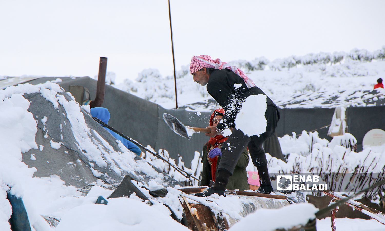 Displaced Syrians clear accumulated snow off the roof of their tents following snowstorms that hit the Sheikh Bilal camp in Rajo area of Afrin district, northern Aleppo - 20 January 2022 (Enab Baladi / Malek al-Habal)