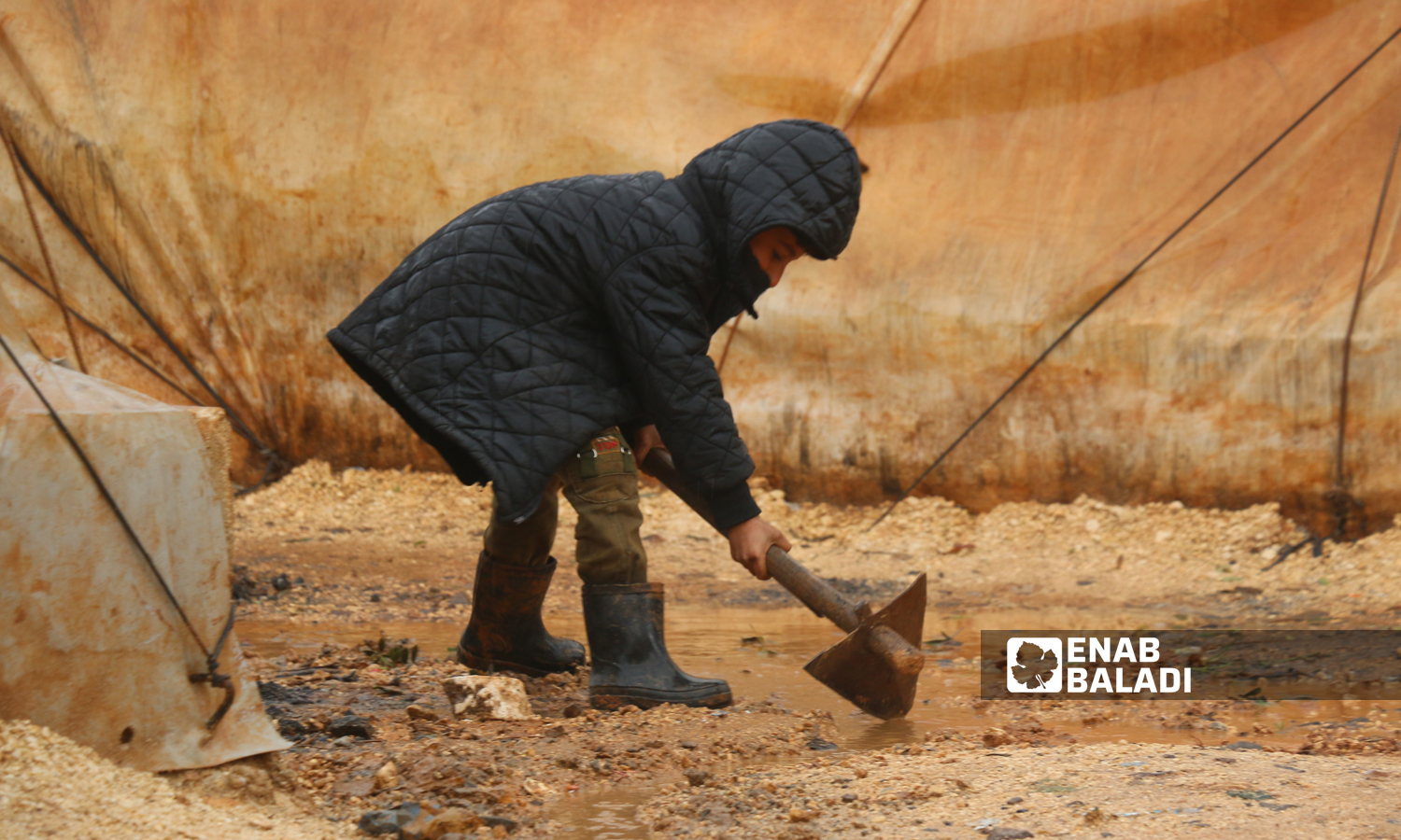 A Syrian displaced child digging a rainwater drain in one of the camps of Idlib countryside - December 2021 (Enab Baladi/Iyad Abdul Jawad)