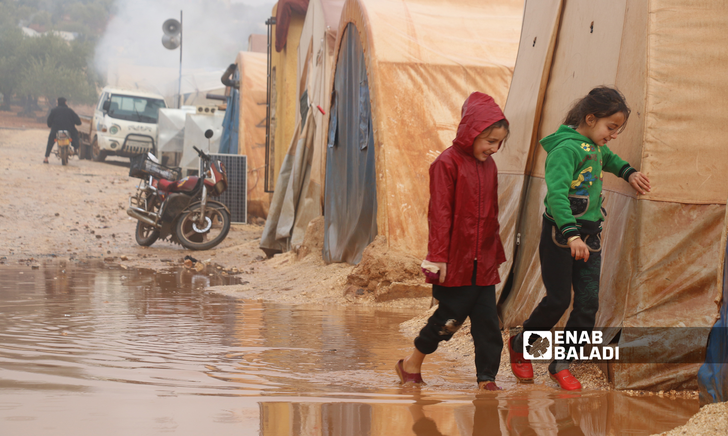 Two Syrian children walking to their tent through a rainwater puddle in the displacement camps of Idlib countryside - December 2021 (Enab Baladi/Iyad Abdul Jawad)