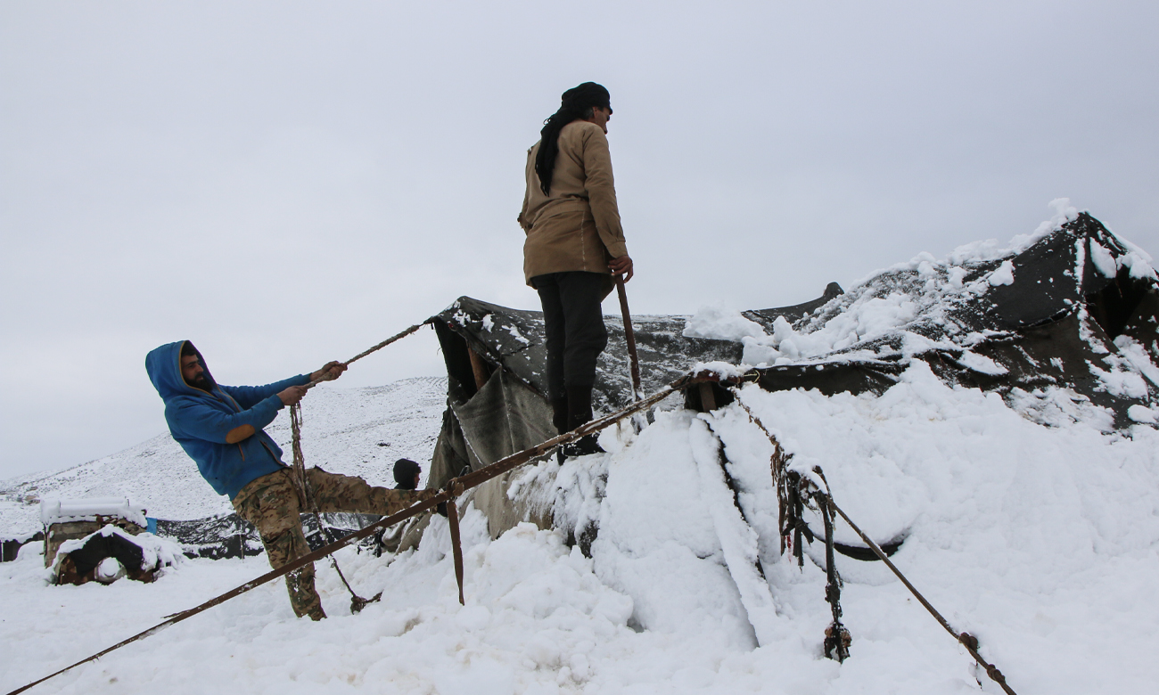 Displaced Syrians clearing accumulated snow off the roof of their tents following snowstorms that hit the Sheikh Bilal camp in Rajo area of Afrin district, northern Aleppo - 20 January 2022 (Enab Baladi / Malek al-Habal)