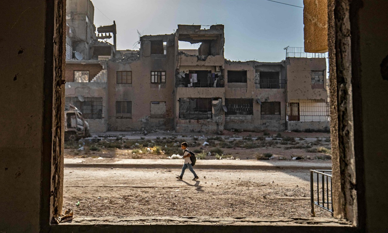 A Syrian student on his way to school passing through war-damaged buildings in the northeastern city of Raqqa - 23 September 2021 (AFP)