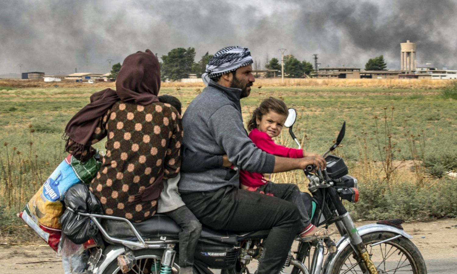 Members of a Syrian family use a motorcycle to flee the countryside of northeastern Ras al-Ain town towards the west to the town of Tal Tamr in al-Hasakah - 19 October 2019 (AFP via Getty Images)