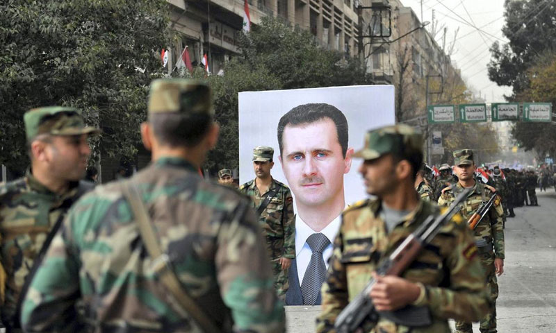 Syrian soldiers passing by a picture of the Syrian regime’s president, Bashar al-Assad, on the first anniversary of his forces’ takeover of Aleppo – 21 December 2017 (AFP)