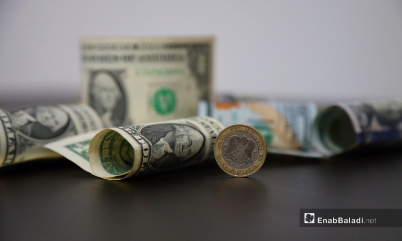 A 25 Syrian pound coin, out of circulation, and US dollar banknotes (Enab Baladi / Zeinab Masri)