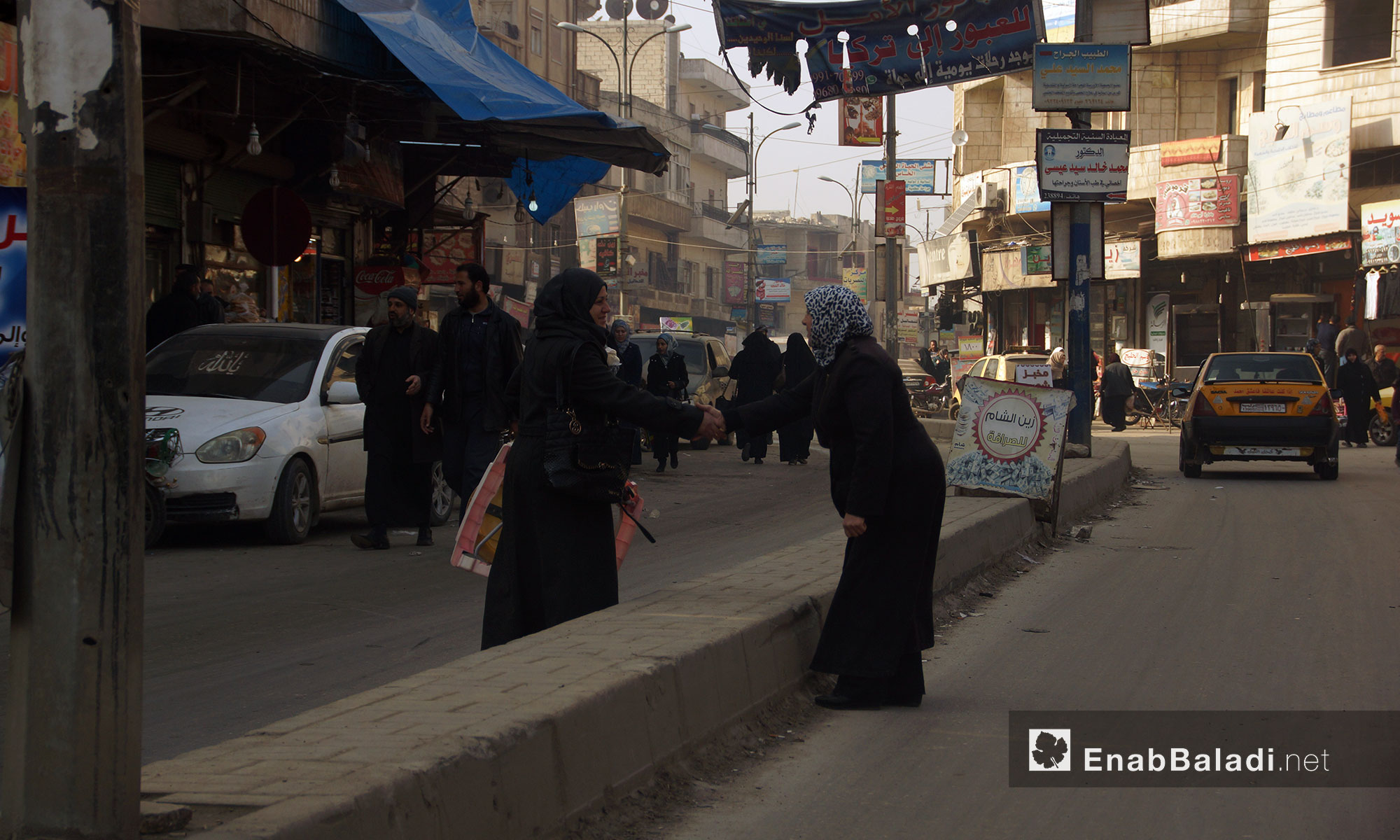 Two women shake hands in a market in the city of Idlib – 13 January 2018 (Enab Baladi)