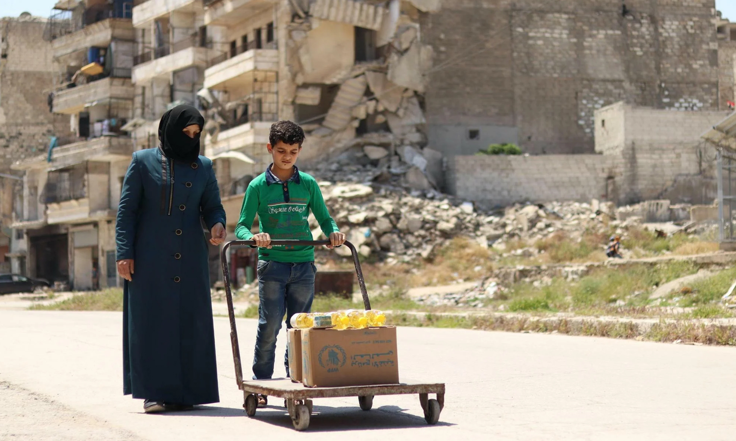 A displaced Syrian woman carrying a humanitarian aid box in Idlib city, northwest Syria - 19 February 2020 (AFP)