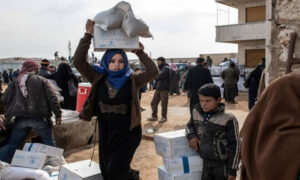 A displaced Syrian woman carrying an aid box