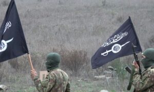 Two fighters carrying the banner of the Hurras al-Din group in the countryside of Idlib (Sham al-Ribat Media)