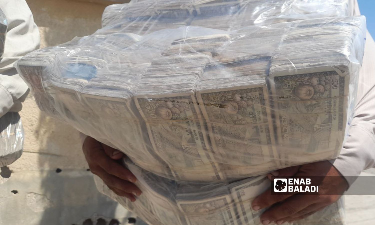A man carries bundles of 500-SYP banknotes in northeastern Raqqa city- 2022 (Enab Baladi / Hussam al-Omar)