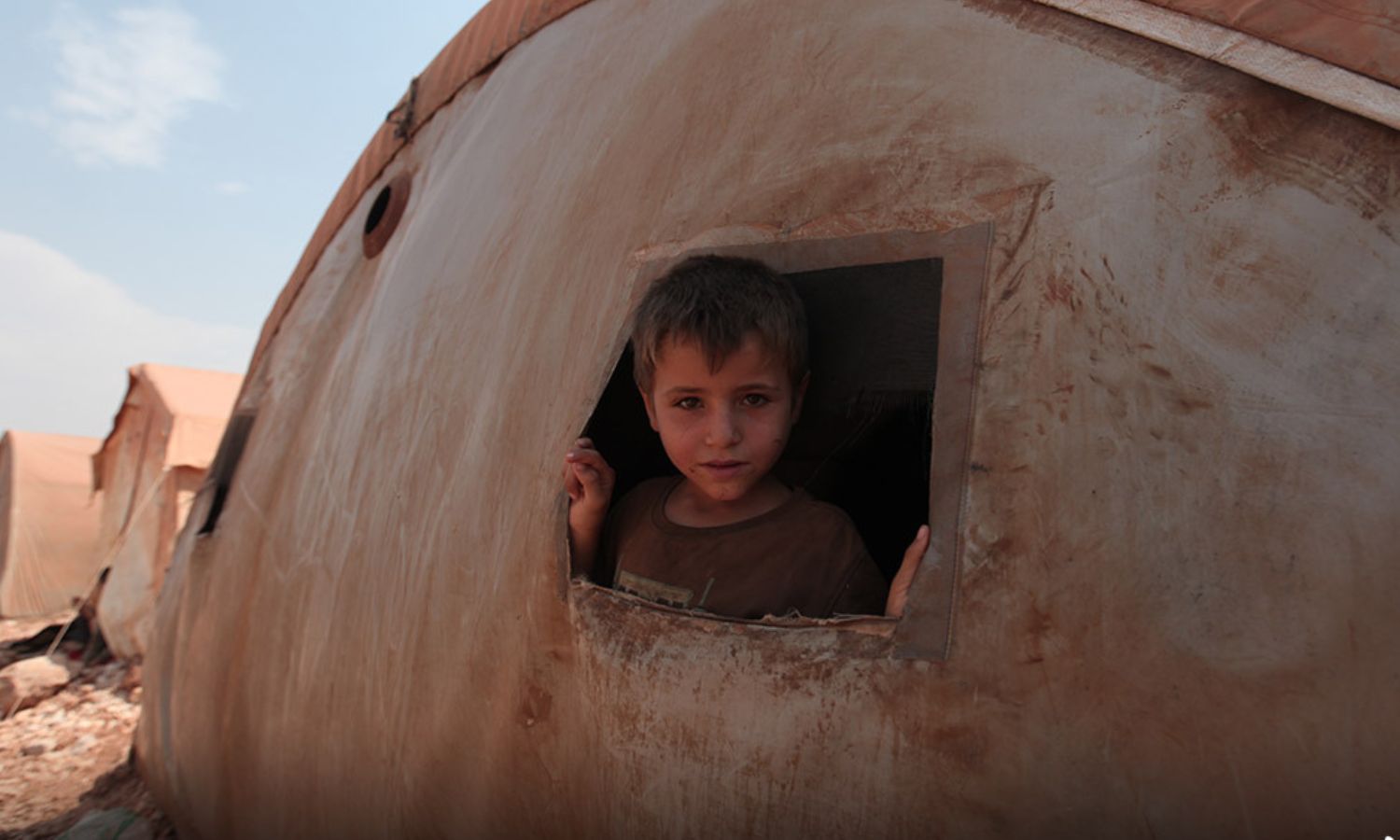 An IDP child poses from the window of his tent in the al-Tah camp in northern Idlib region (Noon Post)