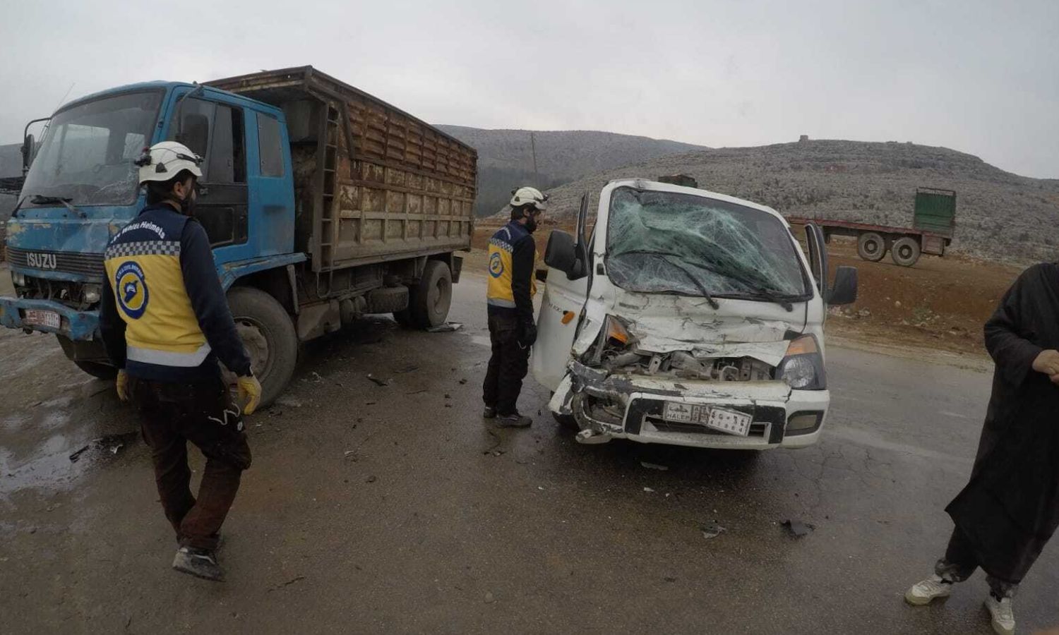 Two Civil Defense volunteers next to a car damaged in a crash accident in northwestern Syria - 22 December 2022 (Syria Civil Defense/Facebook)