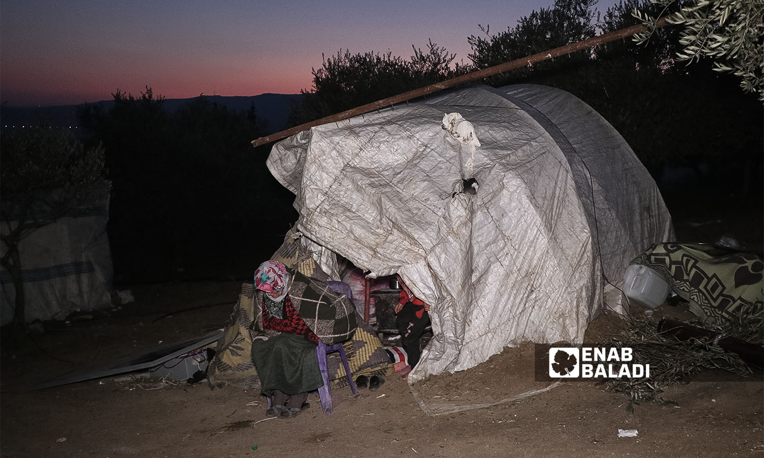 A woman displaced from her home due to the earthquake that hit northwestern Syria spreads out on agricultural land in the village of al-Hamziya in the countryside of Salqin, northern Syria - February 12, 2023 (Enab Baladi/Mohammad Nasan Dabel)