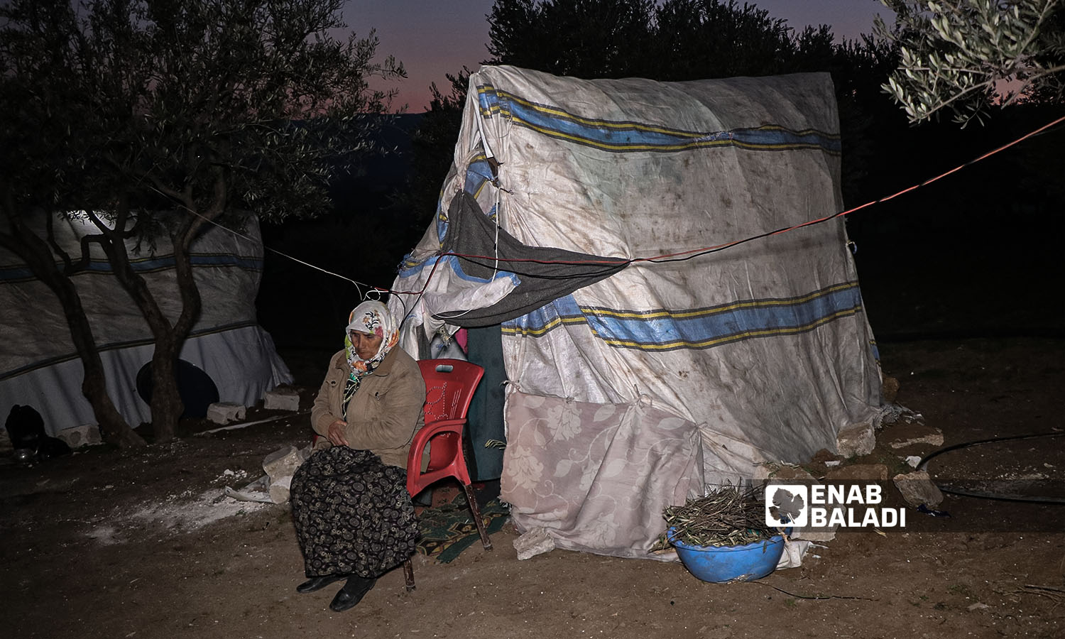 A woman displaced from her home due to the earthquake that struck northwestern Syria, stranded across agricultural land in the village of al-Hamzia in the countryside of Salqin, northern Syria - February 12, 2023 (Enab Baladi/Mohammad Nasan Dabel)