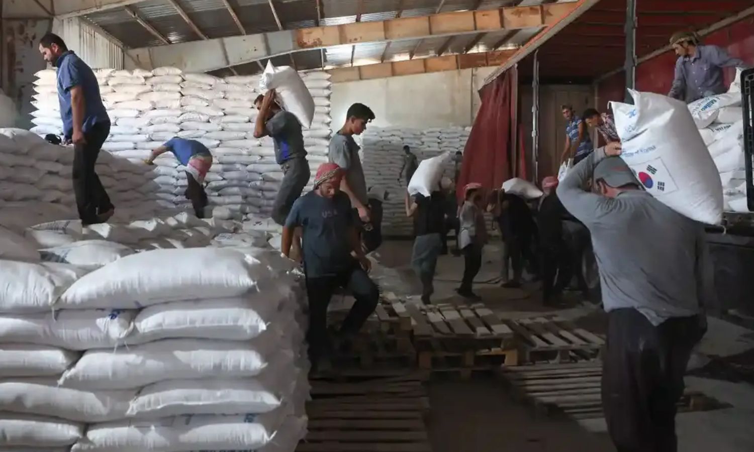 Workers unloading bags of aid in a warehouse near the Bab al-Hawa border crossing - July 10, 2023 (AFP)