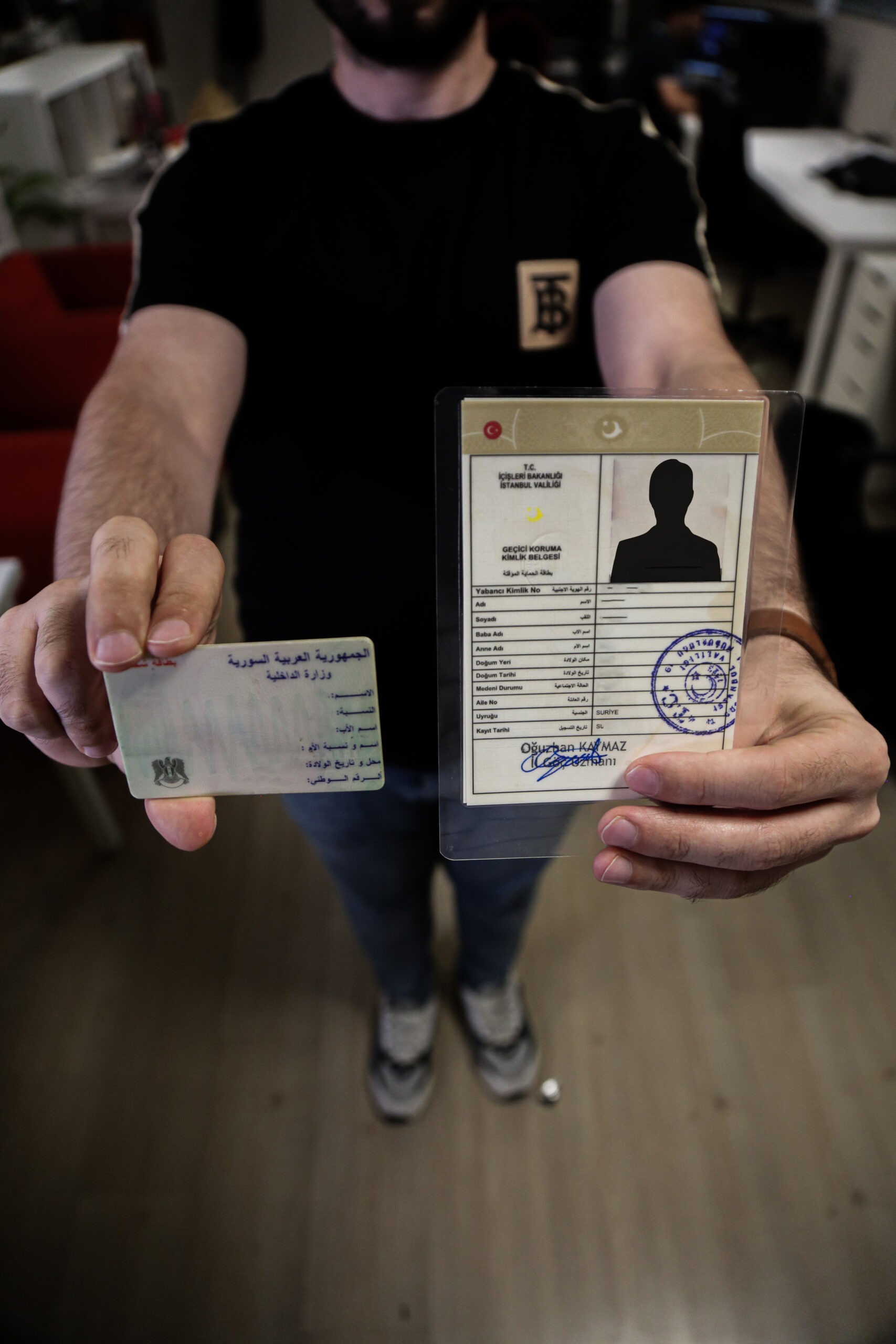 A Syrian refugee holding a temporary protection document (Kimlik) in Turkey and his Syrian identity card - August 11, 2023 (Enab Baladi)