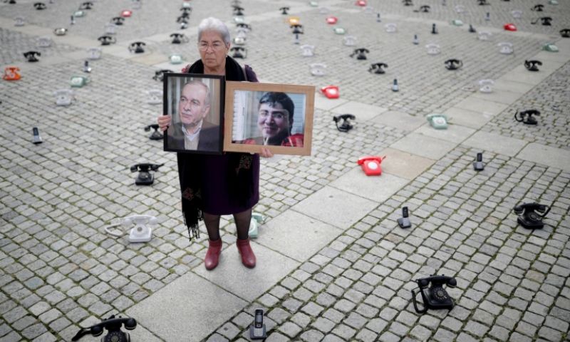 Fadwa Mahmoud holds pictures of her son and husband, who have been forcibly missing since 2012, standing in the middle of an installation that includes 300 landline phones that Syrian families put up in a protest in Germany - August 28, 2021 (Reuters)