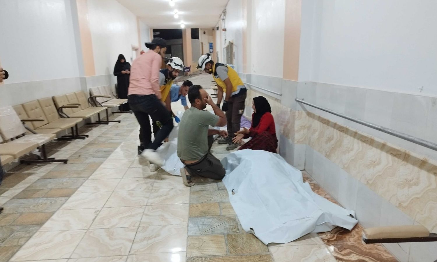 A grieving family in a hospital corridor next to their dead after their home in the town of Kafr Nuran, west of Aleppo, was struck by regime forces - October 5, 2023 (Syria Civil Defense)