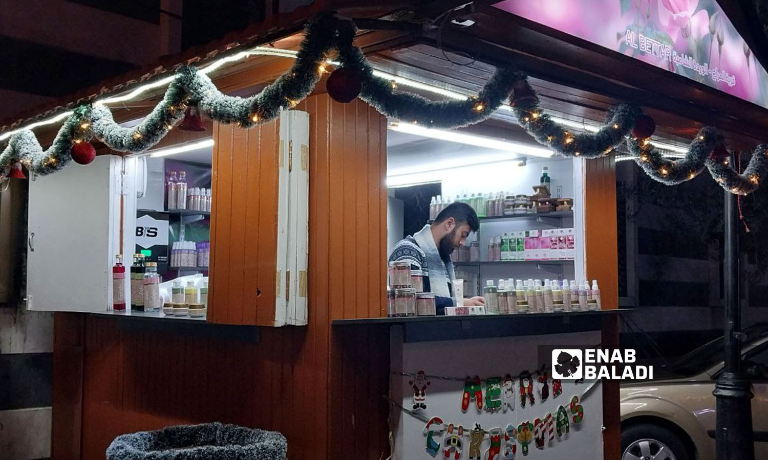 A perfume seller inside a kiosk decorated with Christmas and New Year’s ornaments in Bab Sharqi neighborhood in Damascus - December 26, 2023 (Enab Baladi/Sarah al-Ahmad)
