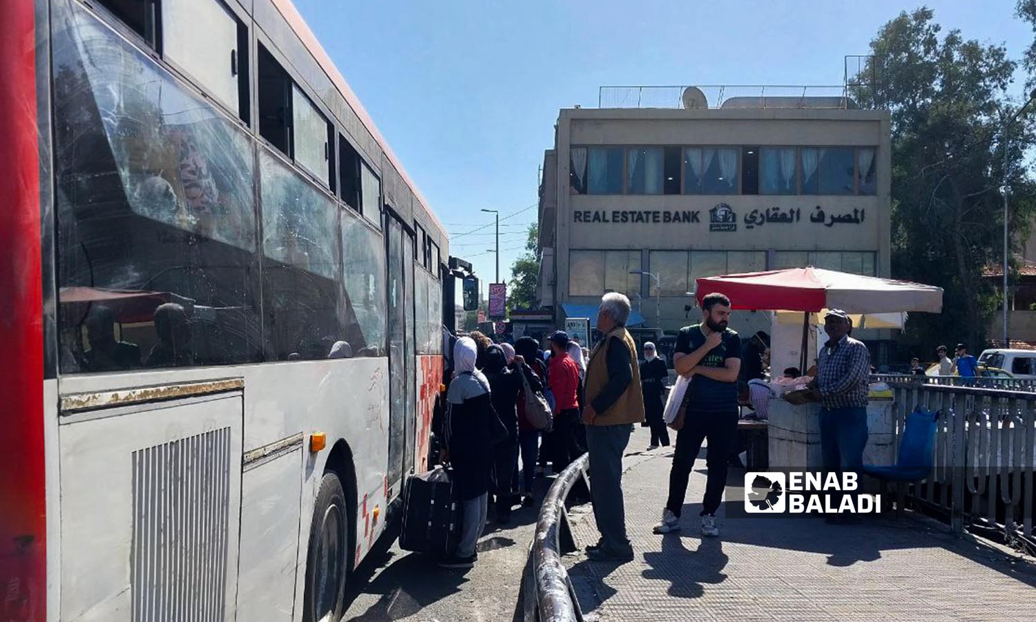 Passengers board a bus near the Real Estate Bank in al-Baramkah area in Damascus city - October 26, 2023 (Enab Baladi/Sarah al-Ahmad)

