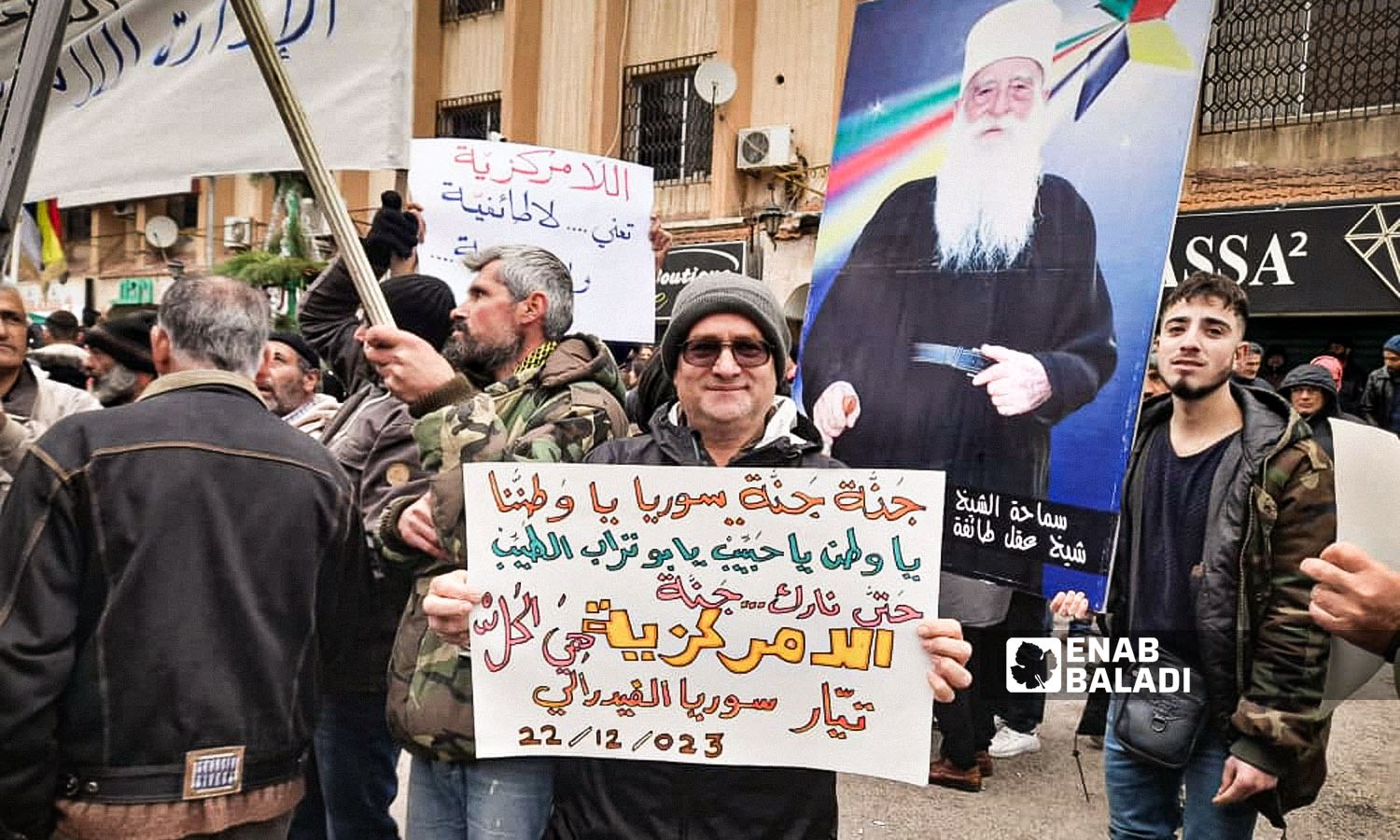 A picture of the Druze spiritual leader, Sheikh Hamoud al-Hinnawi, a supporter of the peaceful movement in As-Suwayda, is raised by demonstrators demanding political change in Syria and the departure of Bashar al-Assad - December 22, 2023 (Enab Baladi)