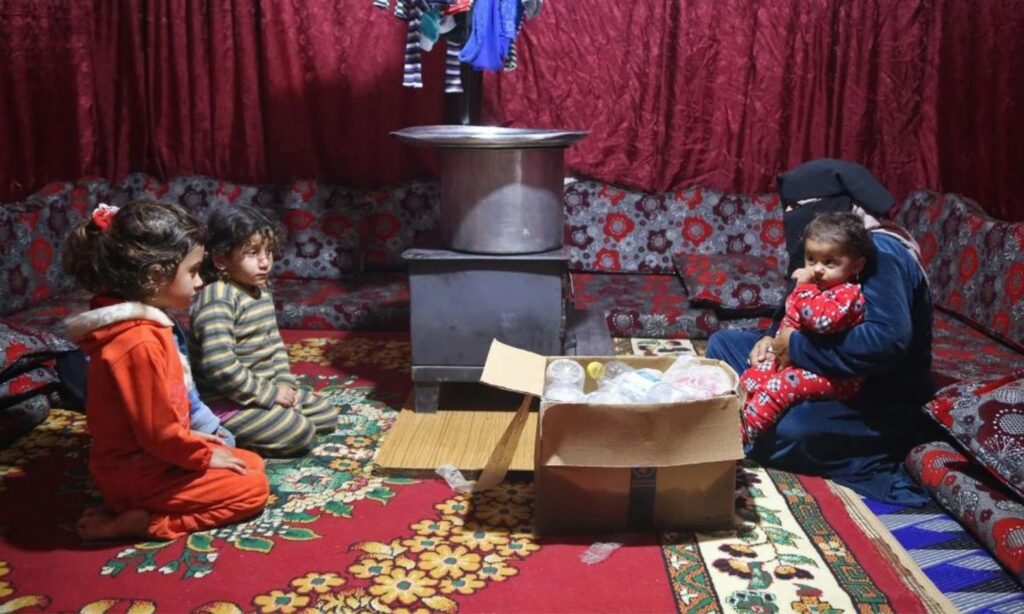 A Syrian woman uses nylon bags and old clothes for heating inside her tent in Idlib - December 12, 2023 (OCHA/Bilal al-Hamoud)