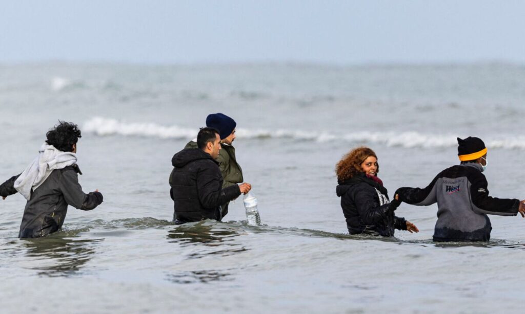 Migrants walking in the sea to reach a boat prepared for smuggling them across the English Channel - April 26, 2024 (AFP)