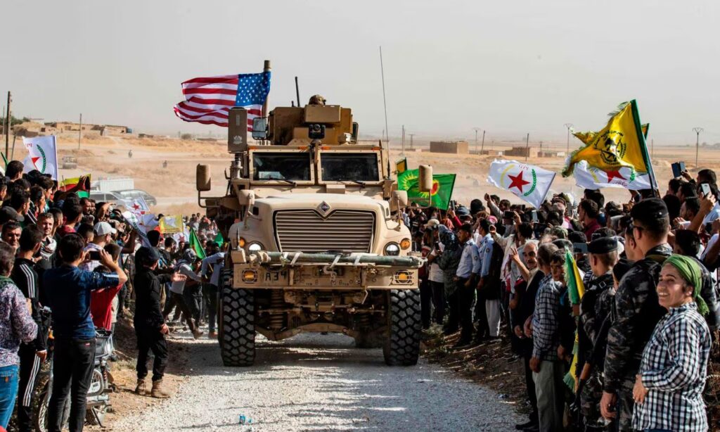 A gathering in the al-Hasakah area of individuals carrying SDF flags around an American vehicle during Turkish military threats to launch a military operation against the SDF - 2019 (AP)