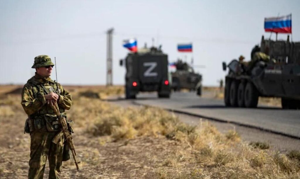 Russian military convoys pass in front of an American soldier in the city of al-Hasakah, northeastern Syria, 2022 (AFP)