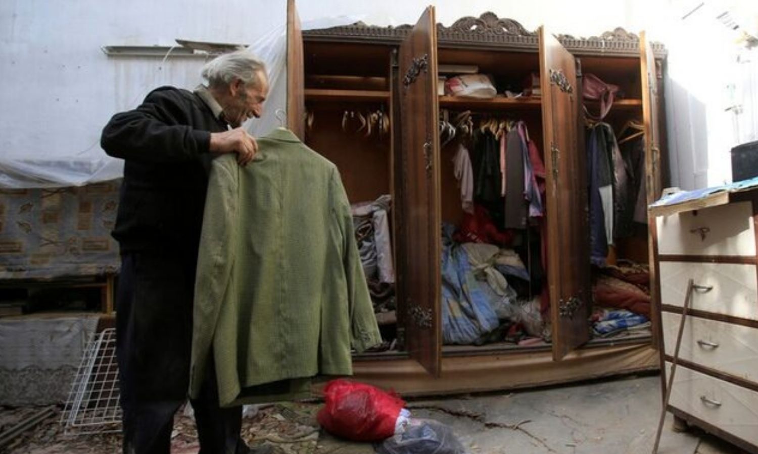 An elderly man carries a piece of clothing in his home located in Jobar neighborhood in Damascus - April 17, 2018 (Reuters)