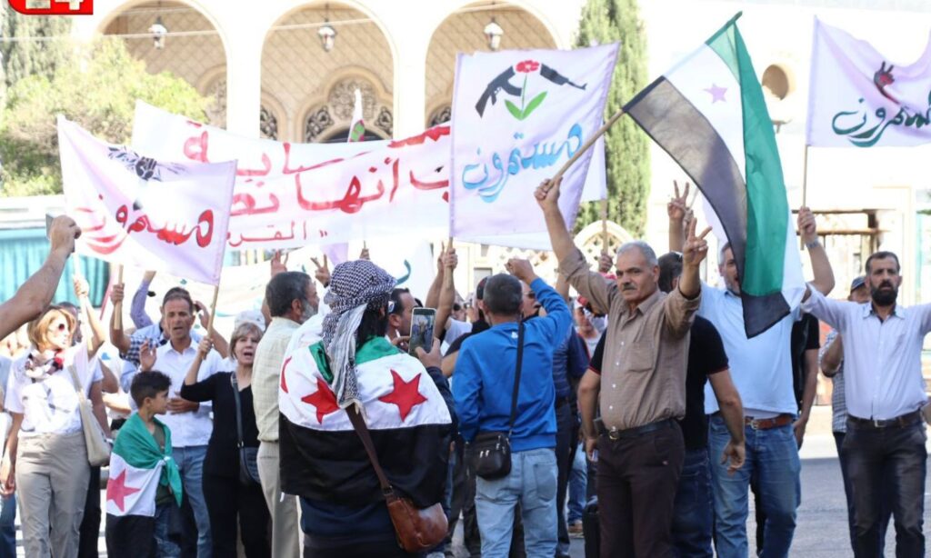 Protesters in al-Karamah Square in As-Suwayda raise the flags of the Syrian revolution and banners affirming the continuation of their protest movement - October 4, 2024 (Suwayda 24)