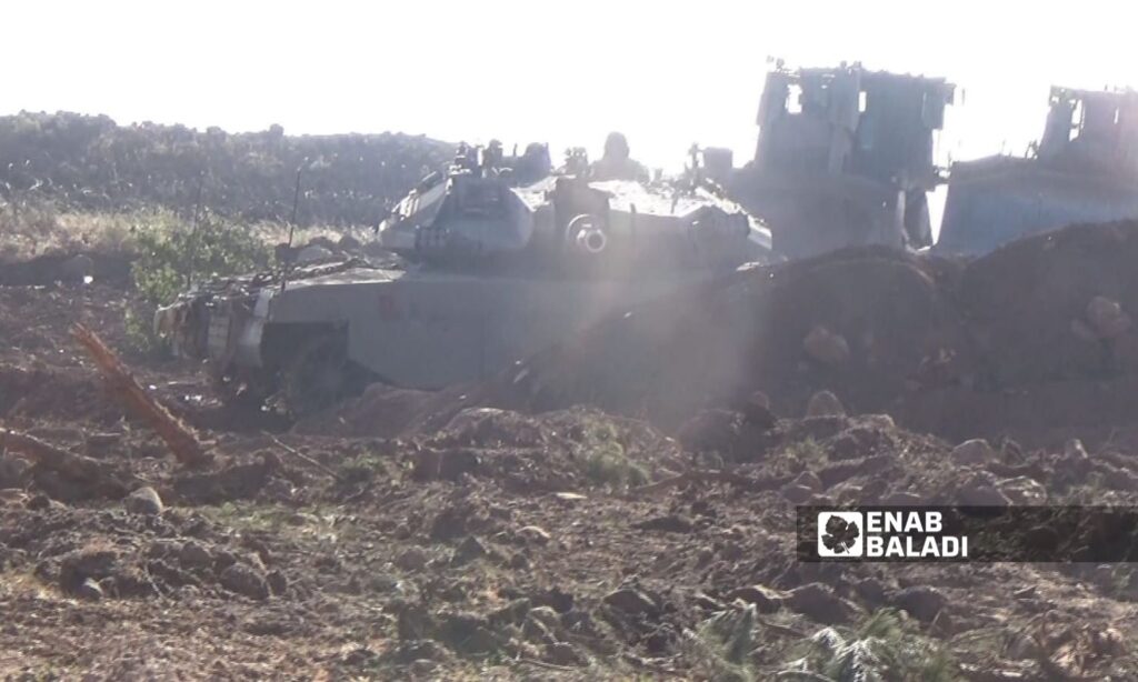 An Israeli Merkava tank secures protection for a military bulldozer during the clearing of agricultural land in southern Quneitra near the occupied Syrian Golan - September 9, 2024 (Enab Baladi/Zain al-Joulani)