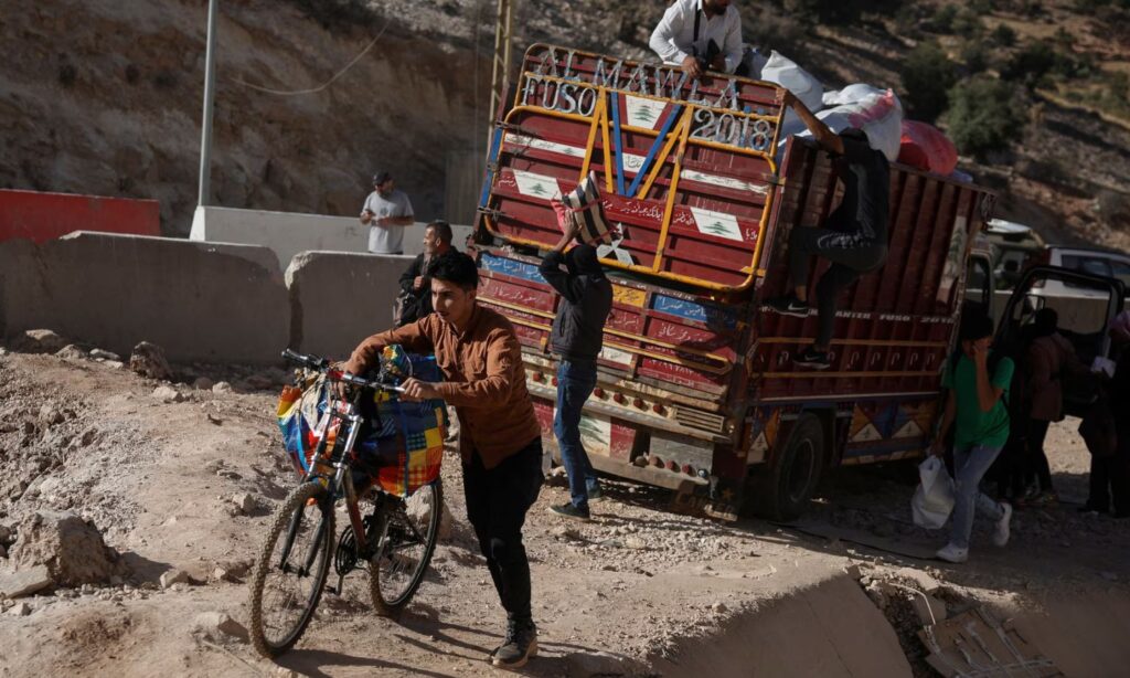 A young man carries his belongings on a bicycle at the al-Masnaa border crossing after Israeli strikes cut off the roads for vehicles - October 14, 2024 (Reuters)