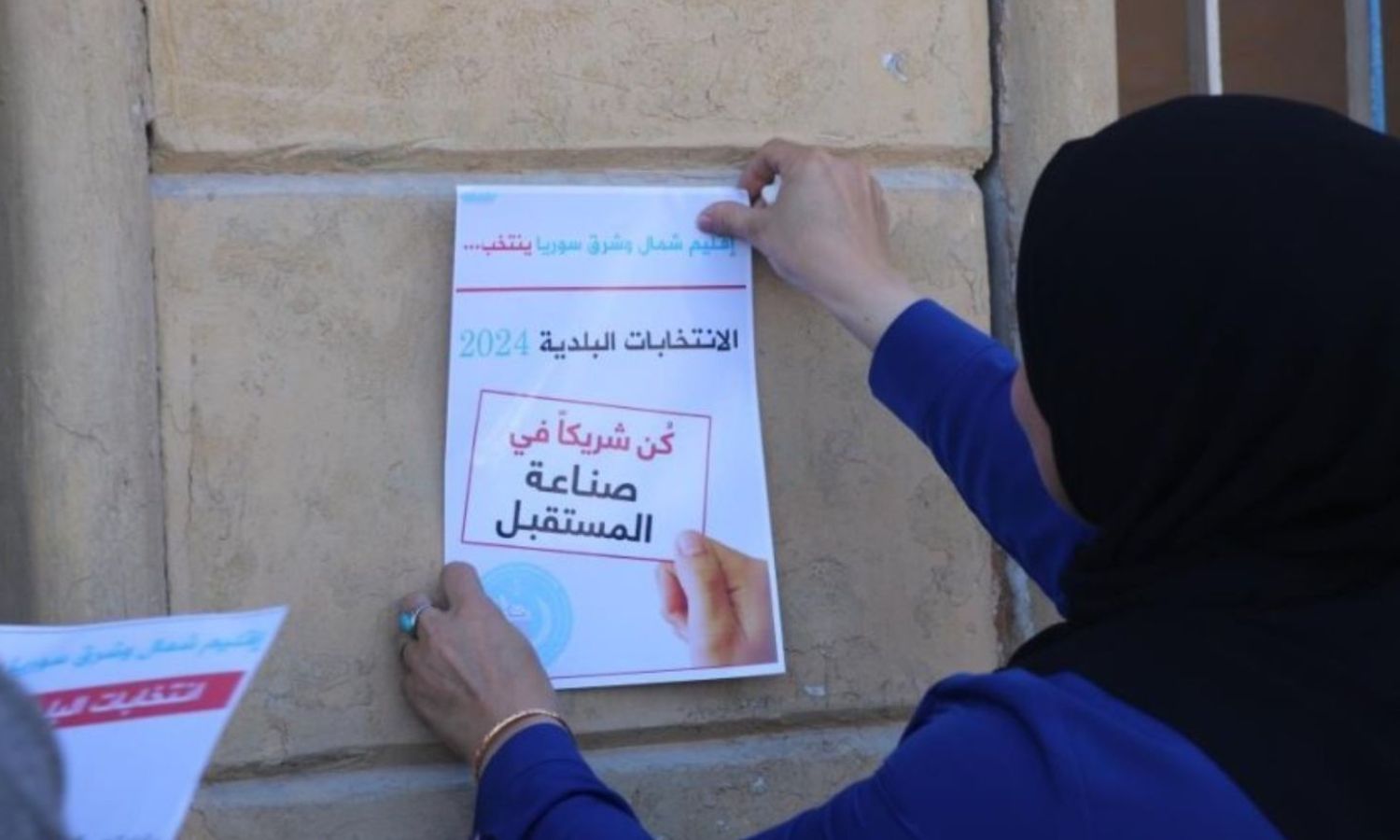 An employee in the Autonomous Administration is distributing promotional posters for local elections in northeastern Syria - June 2, 2024 (Hawar News Agency)
